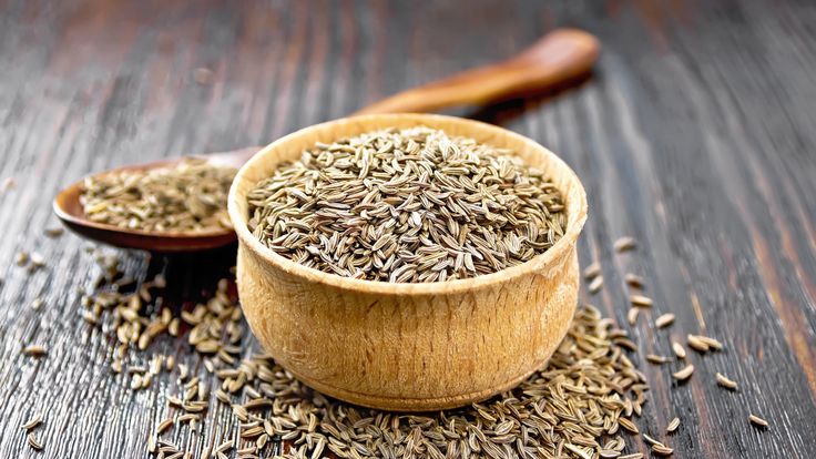 Cumin seeds in bowl and spoon on board